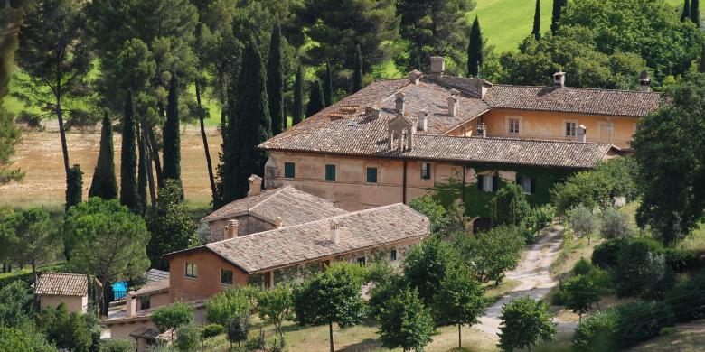 Immagine: Historic stone building with tiled roofs, surrounded by cypress and olive trees on a hillside 